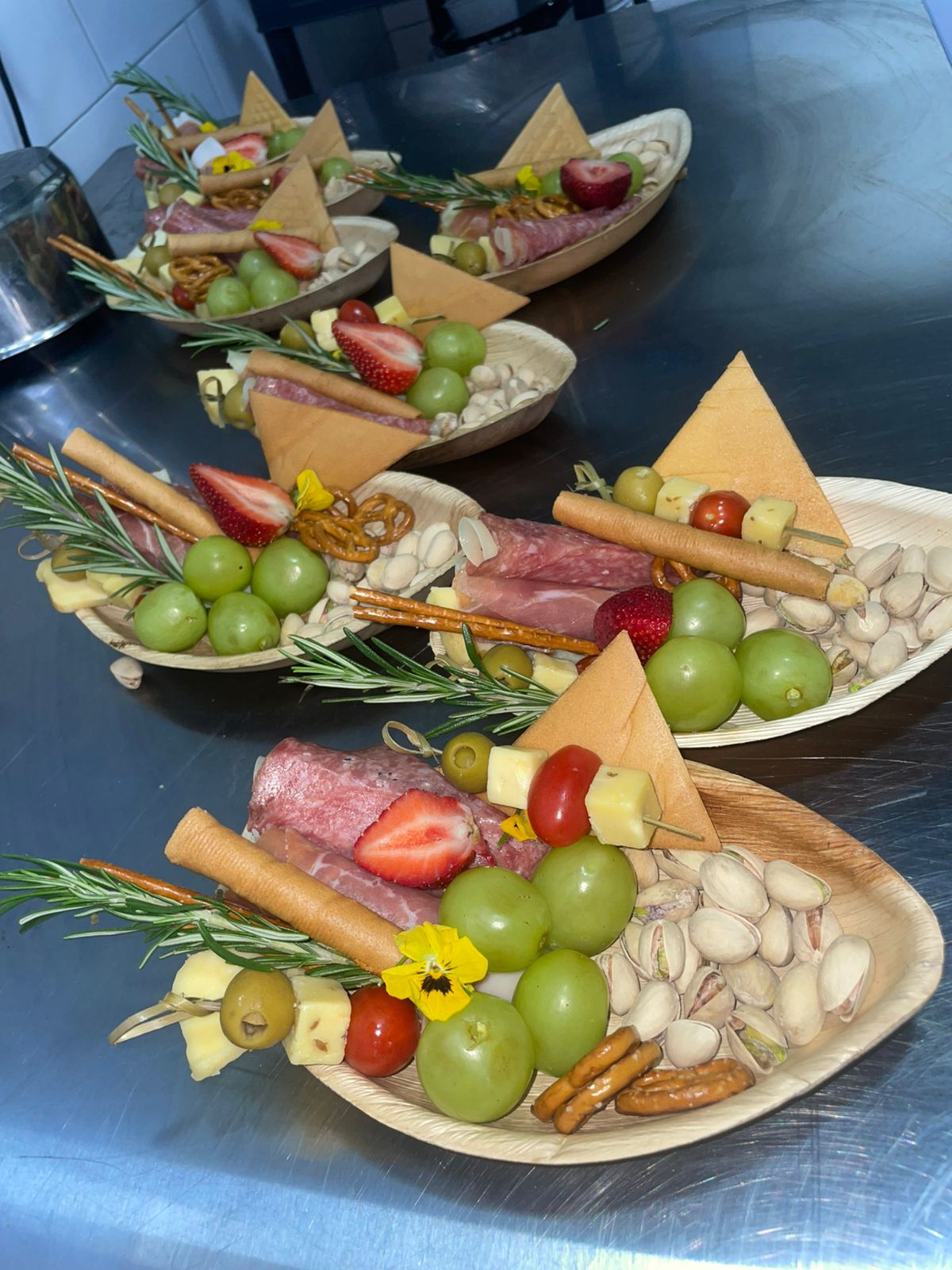 Individual charcuterie boats with salami, cheese skewers, grapes, strawberries, pistachios, pretzels and rosemary