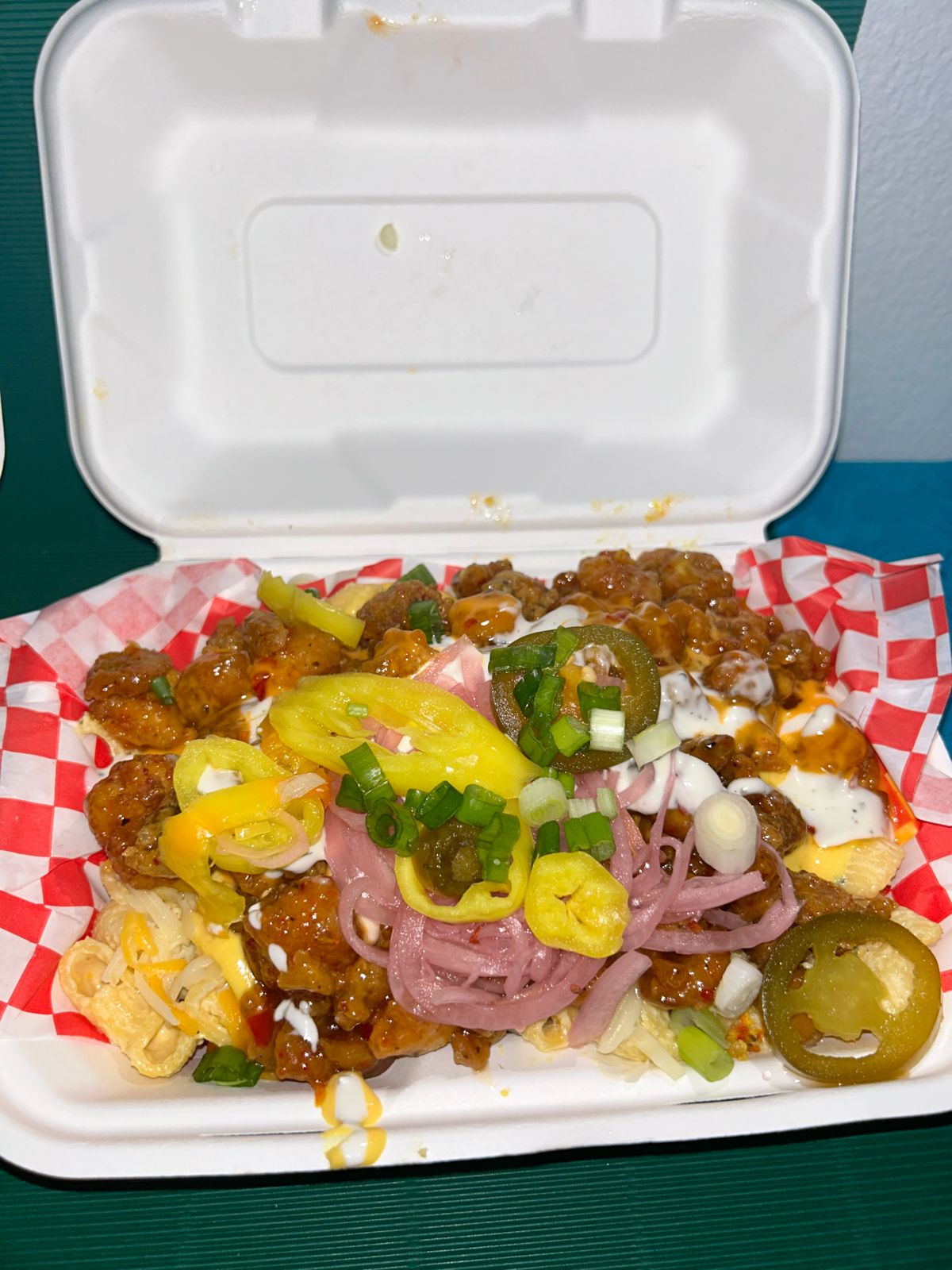 Loaded fries with crispy chicken, cheese sauce, pickled onions, jalapeños and banana peppers in a takeaway box