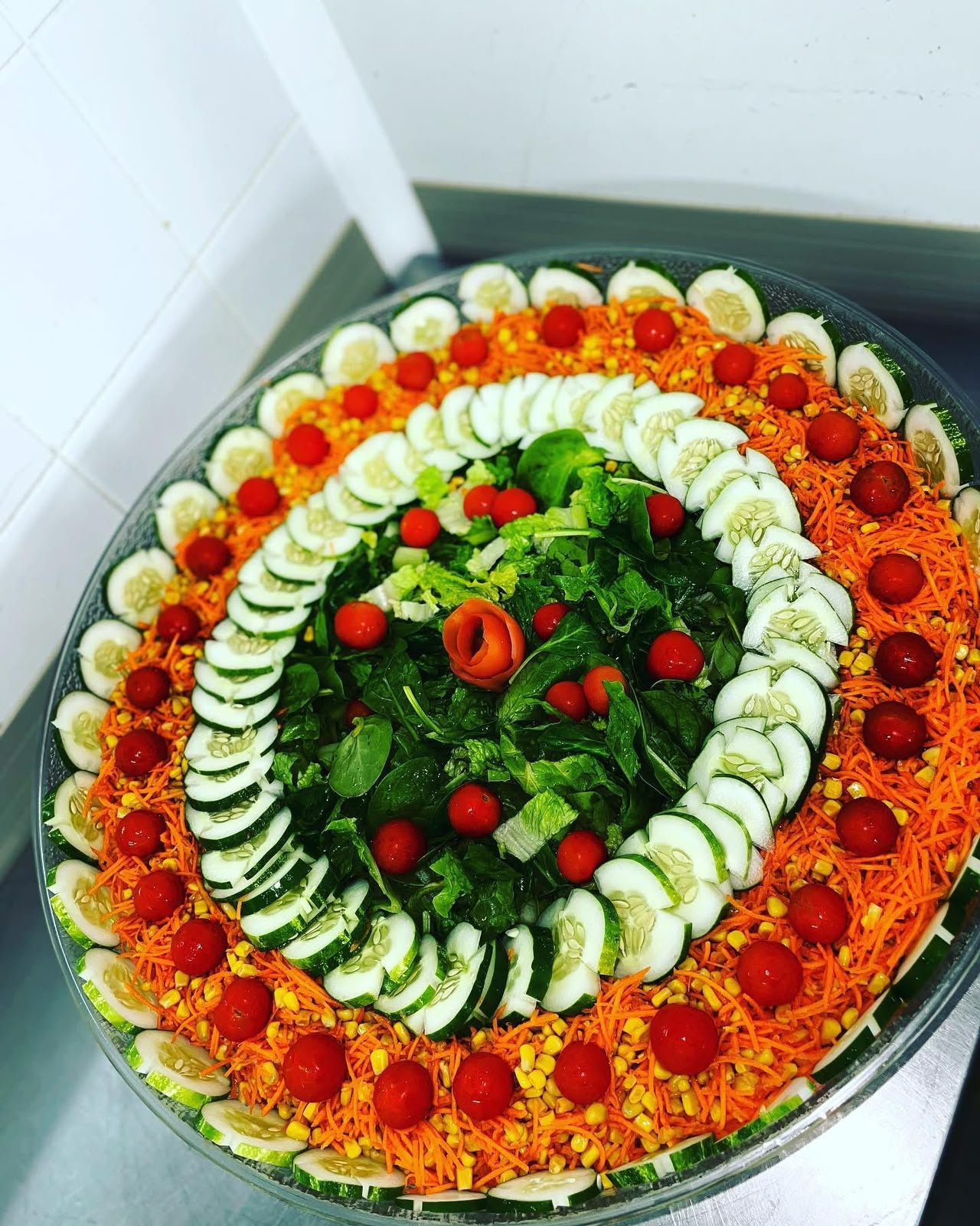 Large garden salad platter arranged in rings of cucumber, carrot, corn, tomato and greens