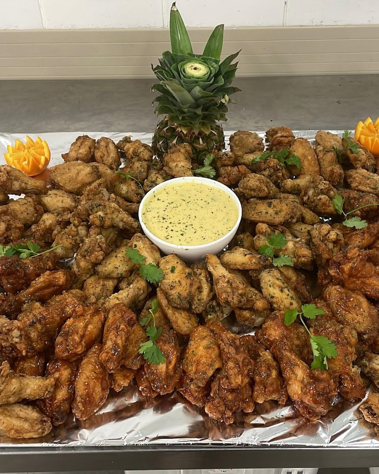 Large platter of seasoned and glazed chicken wings with a creamy dipping sauce and carved pineapple
