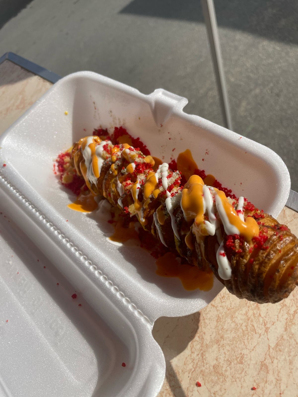 Spiral tornado potato on a skewer drizzled with cheese sauce, aioli and hot chip crumbs