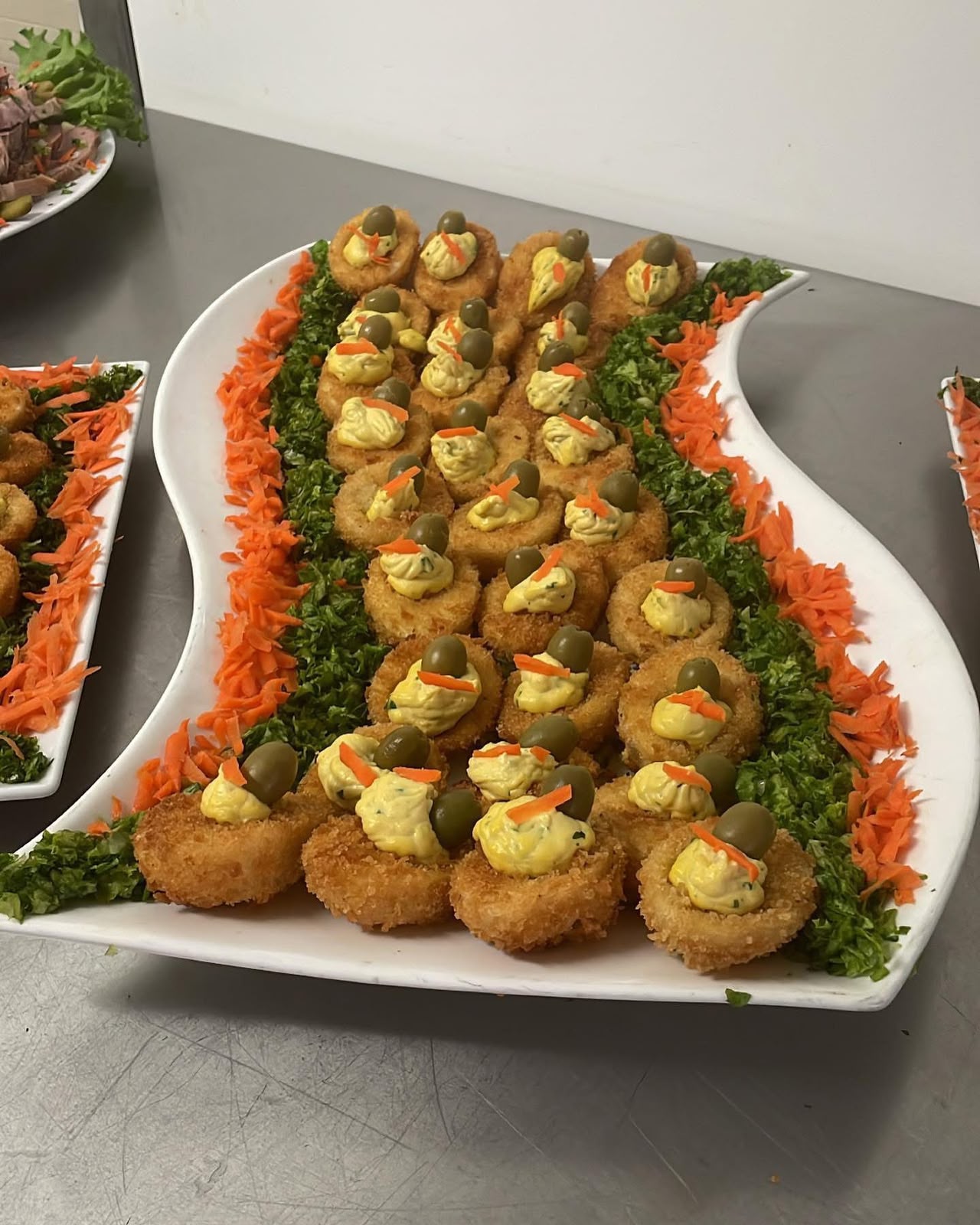 White serving platter of crisp fried canapés piped with herb aioli and topped with olives