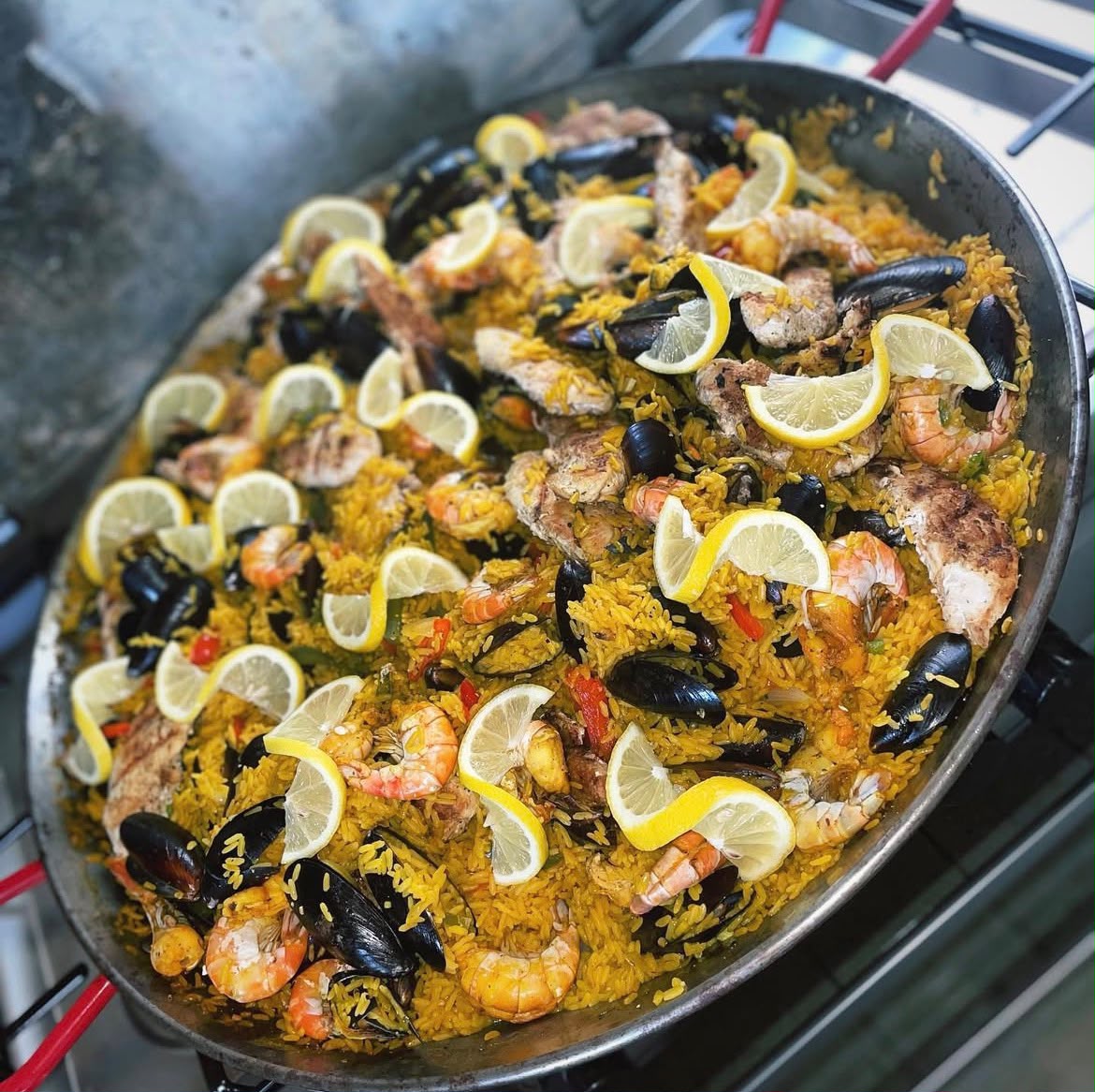 Large paella pan with saffron rice, shrimp, mussels, chicken and lemon wedges